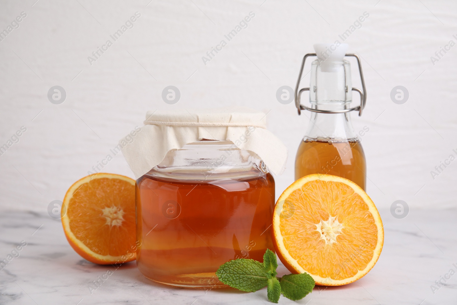 Photo of Tasty kombucha, orange and mint on white marble table