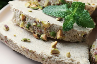 Photo of Pieces of tasty halva with pistachios and mint on table, closeup