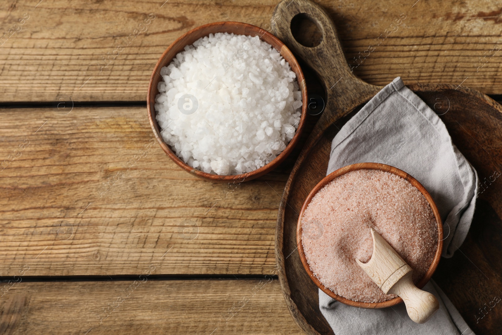 Photo of Different natural salt on wooden table, flat lay. Space for text