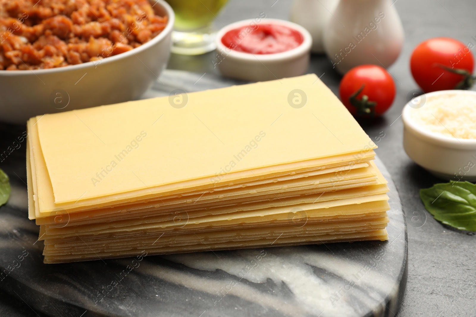 Photo of Cooking lasagna. Board with pasta sheets on dark table, closeup