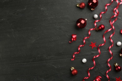 Photo of Shiny serpentine streamers and Christmas balls on black background, flat lay. Space for text
