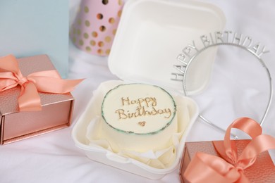 Photo of Delicious decorated cake, gifts and headband on white cloth. Happy Birthday