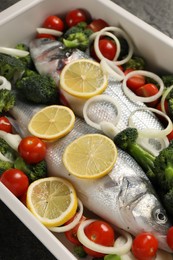 Photo of Raw fish with vegetables and lemon in baking dish on table