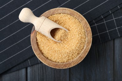 Brown sugar in bowl and scoop on black wooden table, top view