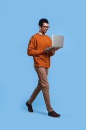 Photo of Happy man with laptop walking on light blue background
