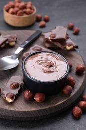 Photo of Bowl with tasty paste, chocolate pieces and nuts on grey table