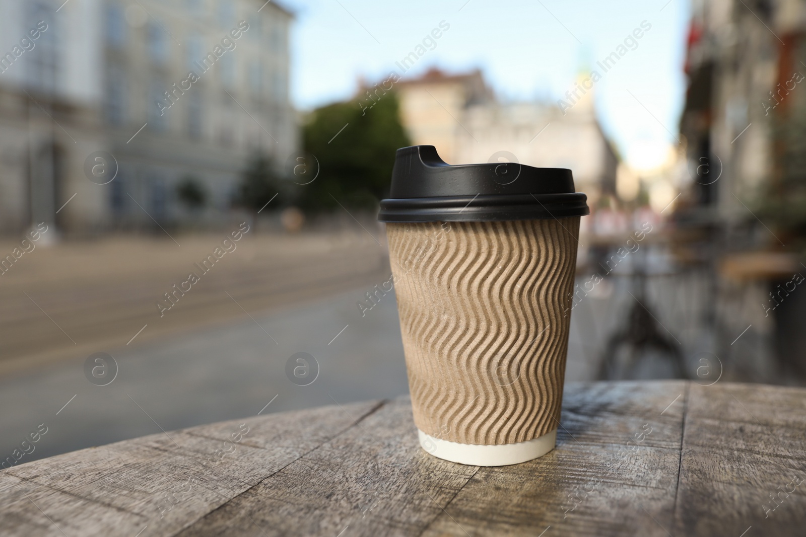 Photo of Cardboard takeaway coffee cup with plastic lid on wooden table in city, space for text