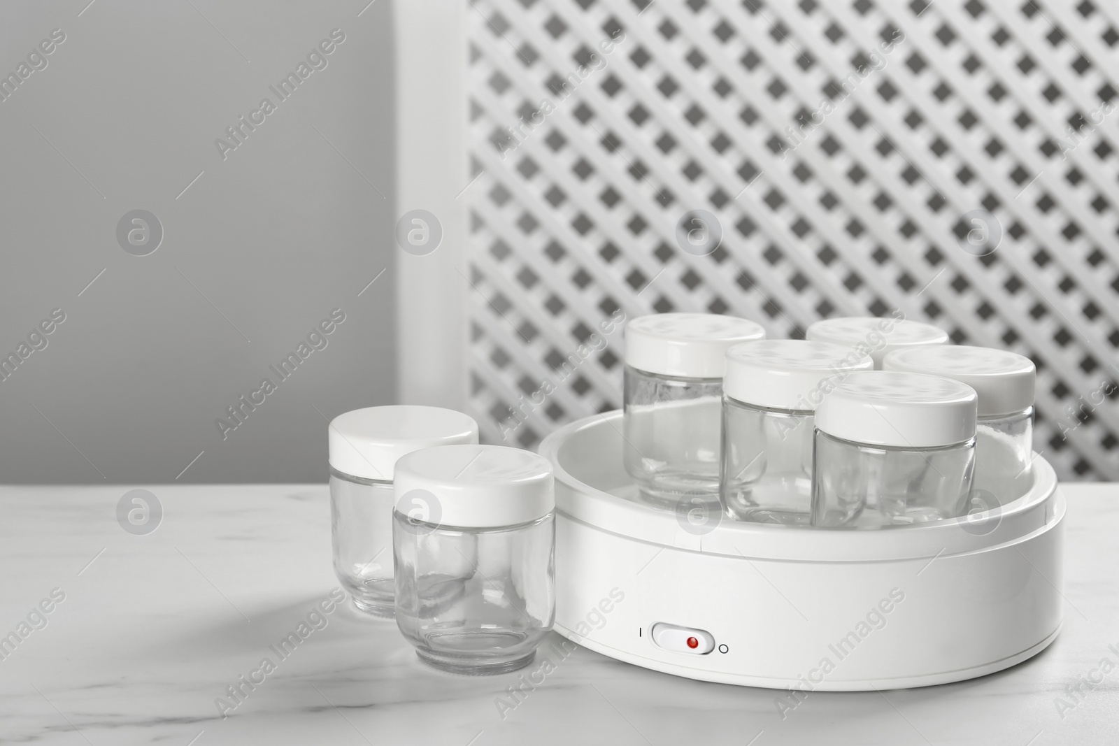 Photo of Modern yogurt maker with empty jars on white table indoors. Space for text