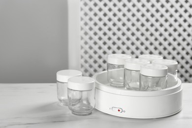 Modern yogurt maker with empty jars on white table indoors. Space for text