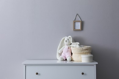 Child's toy and wicker basket on chest of drawers near light grey wall indoors