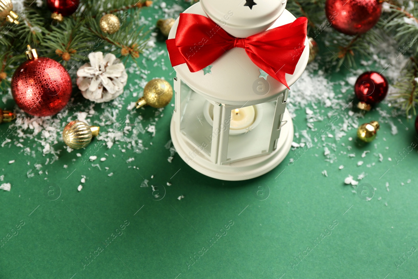 Photo of Christmas lantern with burning candle and festive decor on green background