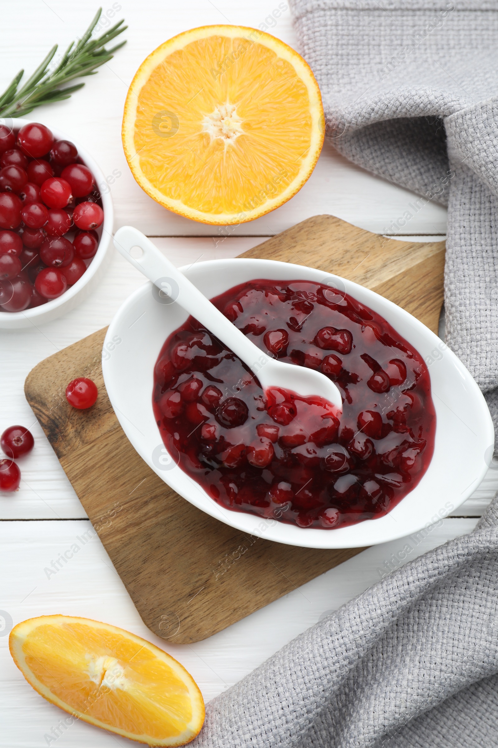 Photo of Tasty cranberry sauce in bowl, fresh berries and orange slices on white wooden table, flat lay