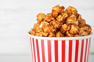 Paper cup with caramel popcorn on light background, closeup