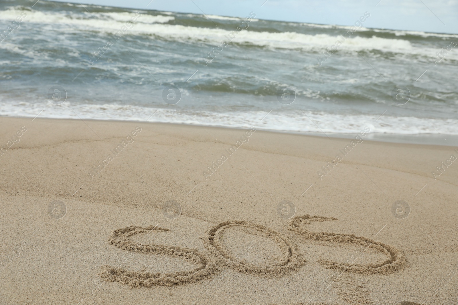 Photo of Message SOS drawn on sand near sea