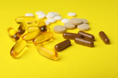 Photo of Different dietary supplements on yellow background, closeup