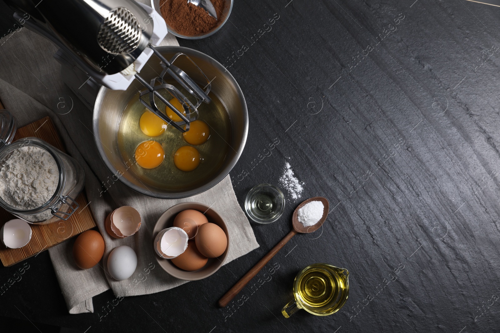 Photo of Making dough. Raw eggs in bowl of stand mixer and ingredients on black table, flat lay with space for text