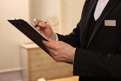 Photo of Man in suit with clipboard indoors, closeup. Professional butler courses