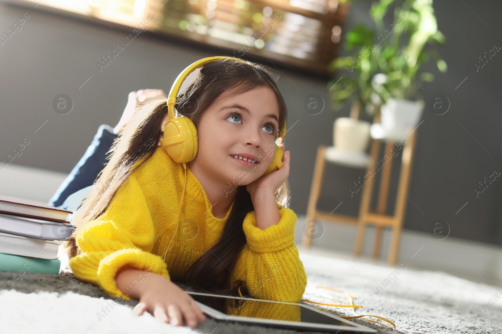 Photo of Cute little girl with headphones and tablet listening to audiobook at home