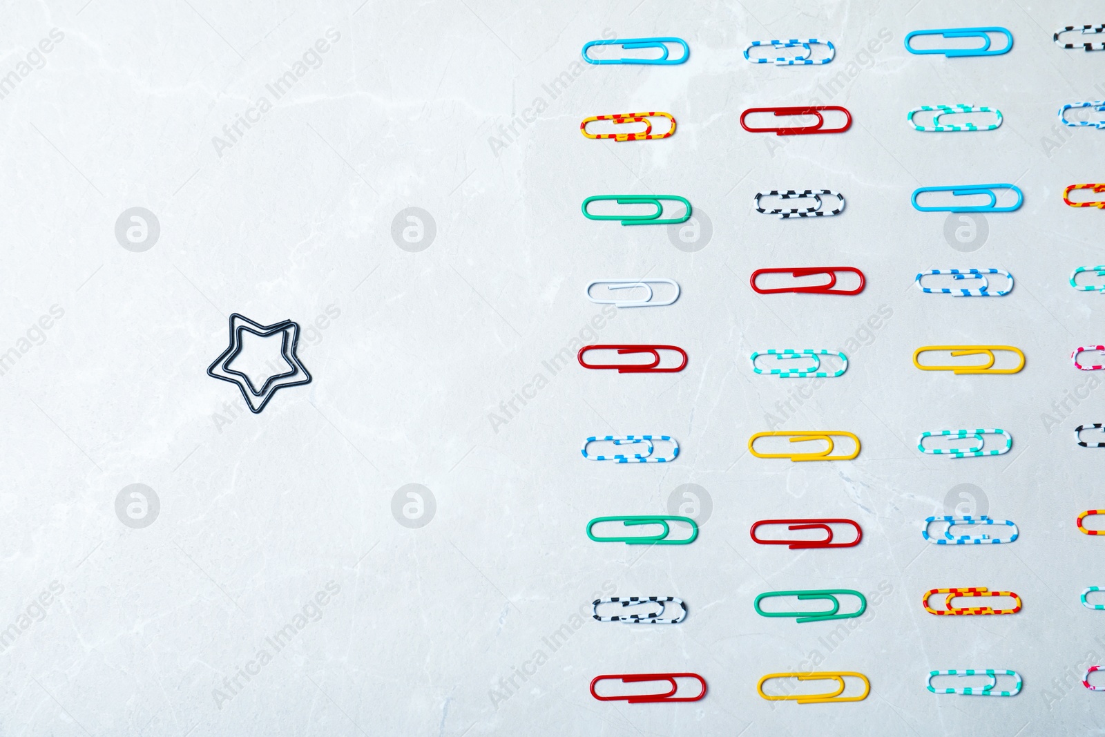 Photo of Different paper clip standing out from others on light background, top view