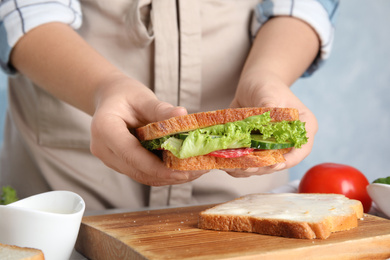 Photo of Woman holding tasty fresh sandwich at table, closeup