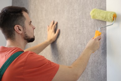 Man hanging stylish gray wallpaper in room