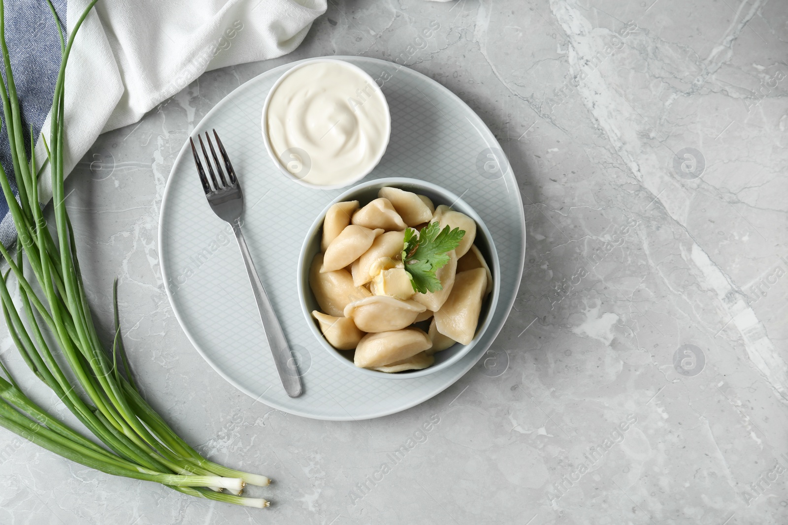 Photo of Delicious cooked dumplings and sour cream on grey marble table, flat lay