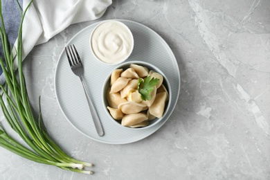 Delicious cooked dumplings and sour cream on grey marble table, flat lay