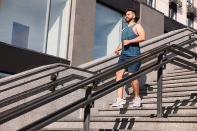 Happy man running down stairs outdoors on sunny day, low angle view. Space for text