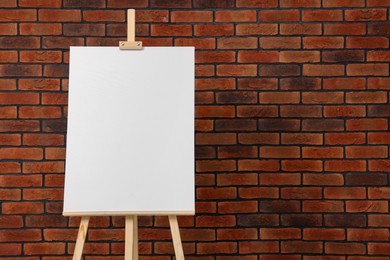 Wooden easel with blank canvas near brick wall. Space for text