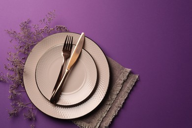 Photo of Stylish table setting. Plates, cutlery, napkin and floral decor on purple background, top view with space for text
