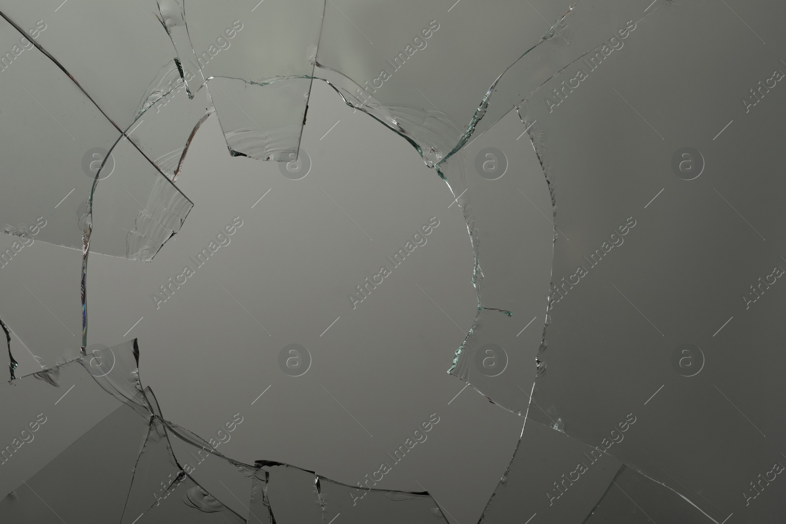 Photo of Closeup view of broken glass with cracks on grey background