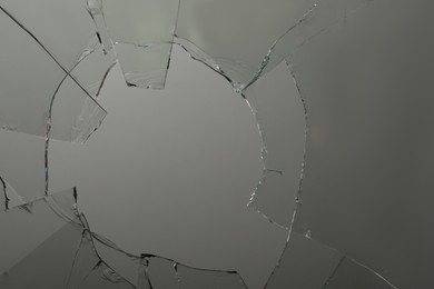 Photo of Closeup view of broken glass with cracks on grey background