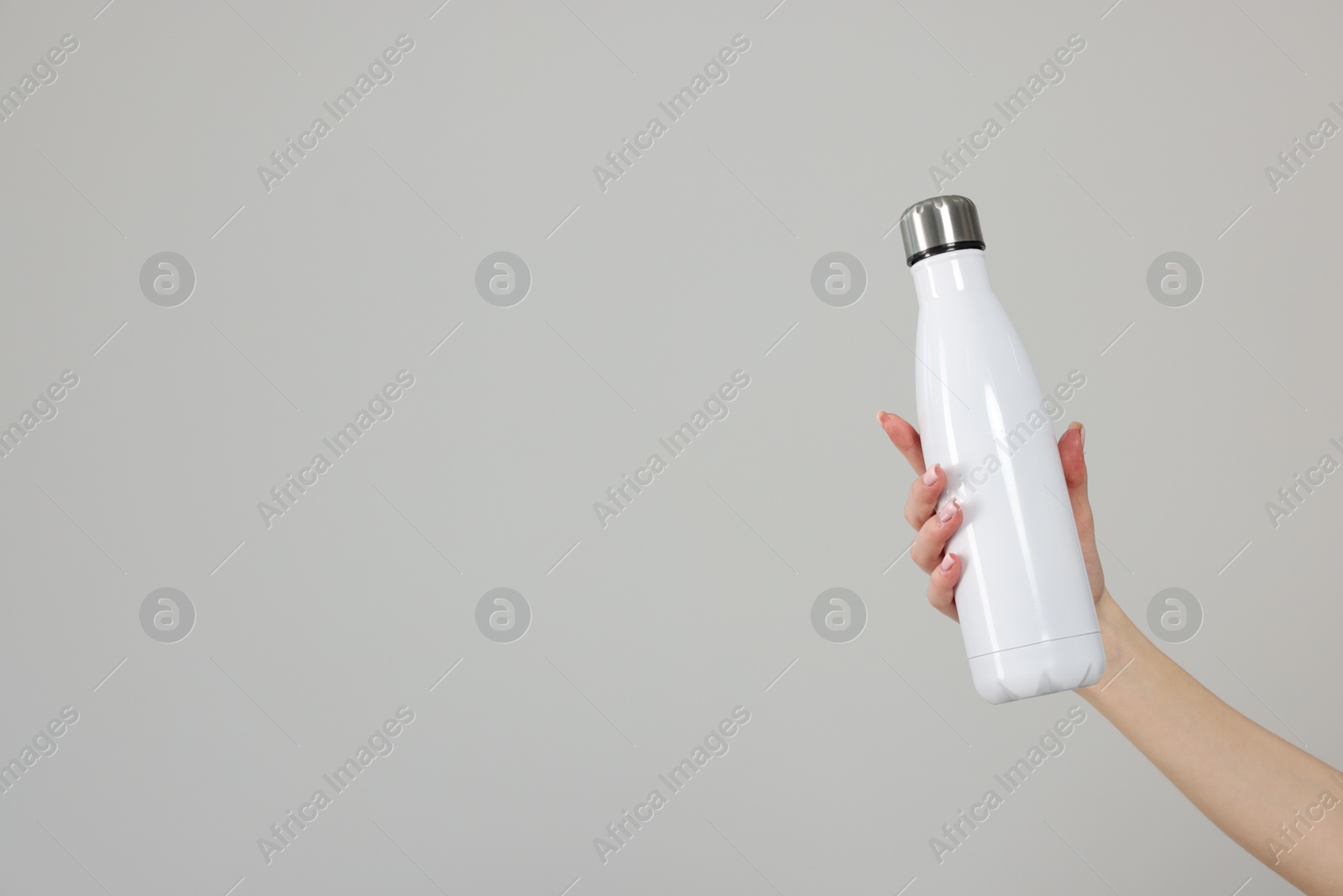 Photo of Woman holding thermos bottle on light grey background, closeup. Space for text