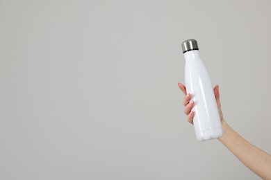 Photo of Woman holding thermos bottle on light grey background, closeup. Space for text