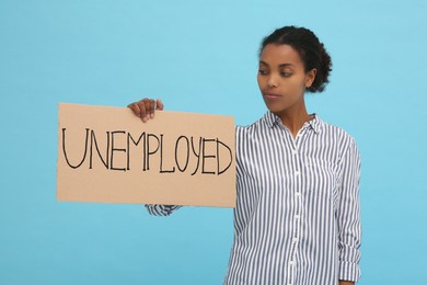 African American woman holding sign with word Unemployed on light blue background