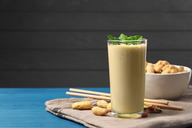 Photo of Glass of tasty banana smoothie with peanuts and mint on light blue wooden table. Space for text