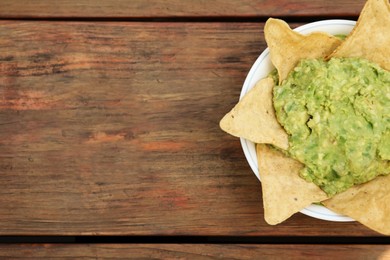 Delicious guacamole made of avocados with nachos on wooden table, top view. Space for text