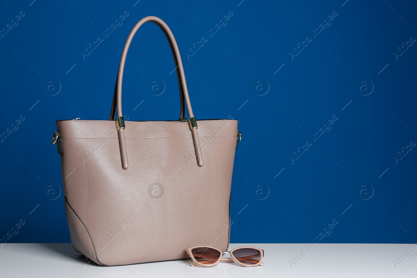 Photo of Stylish woman's bag and sunglasses on white table. Space for text