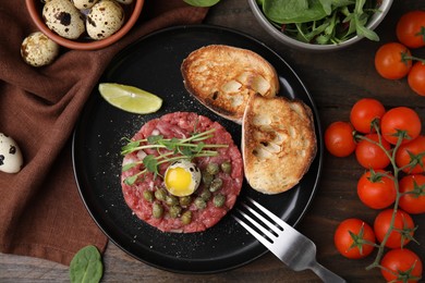 Photo of Tasty beef steak tartare served with quail egg and other accompaniments on wooden table, flat lay