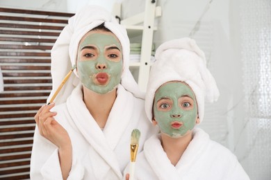 Photo of Young mother and her daughter with facial masks having fun in bathroom