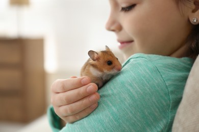 Photo of Little girl holding cute hamster at home, closeup