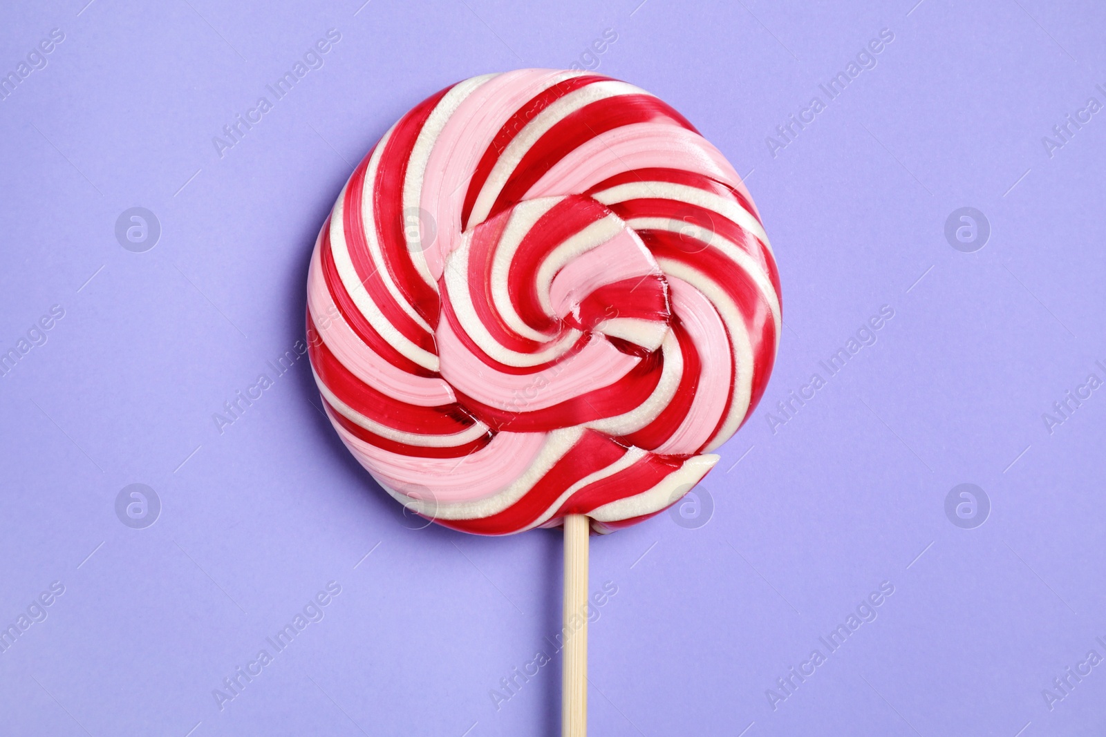 Photo of Stick with colorful lollipop swirl on violet background, top view