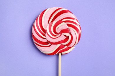Photo of Stick with colorful lollipop swirl on violet background, top view