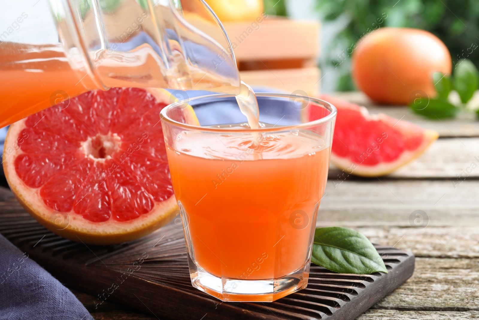 Photo of Pouring delicious grapefruit juice into glass on wooden table