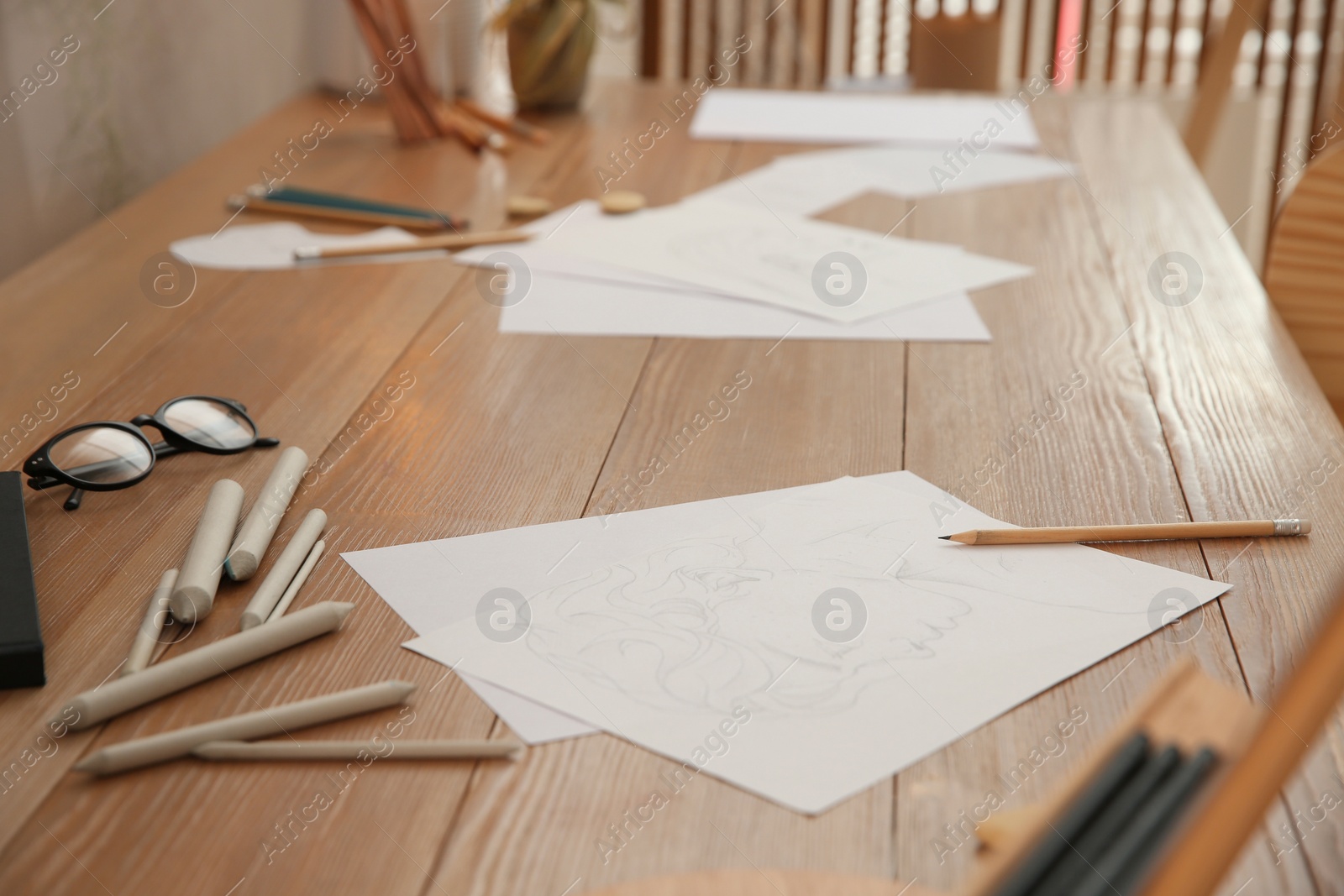 Photo of Male portrait drawing, pencils and glasses on wooden table in art studio