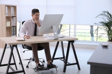 Photo of Man using footrest while working on computer in office