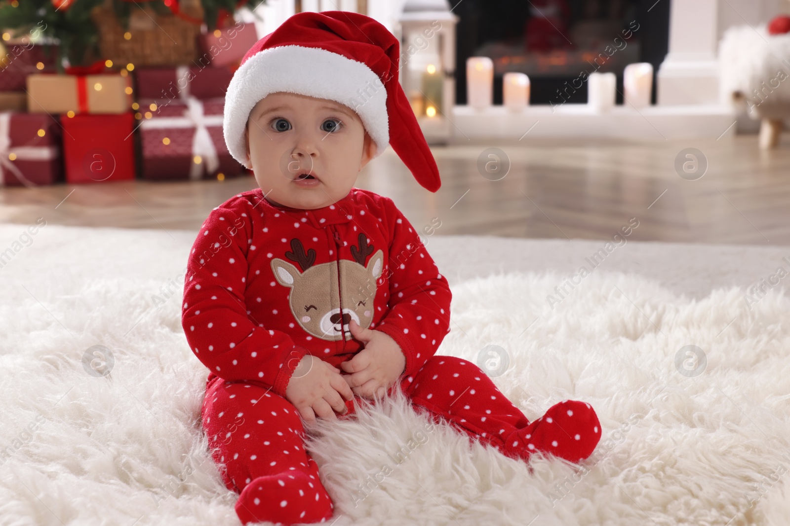 Photo of Baby in Santa hat and bright Christmas pajamas on floor at home