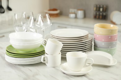 Photo of Clean plates, bowls, cups and glasses on white marble table in kitchen