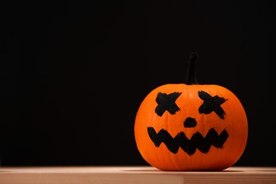 Photo of Halloween celebration. Pumpkin with drawn face on wooden table against black background, space for text