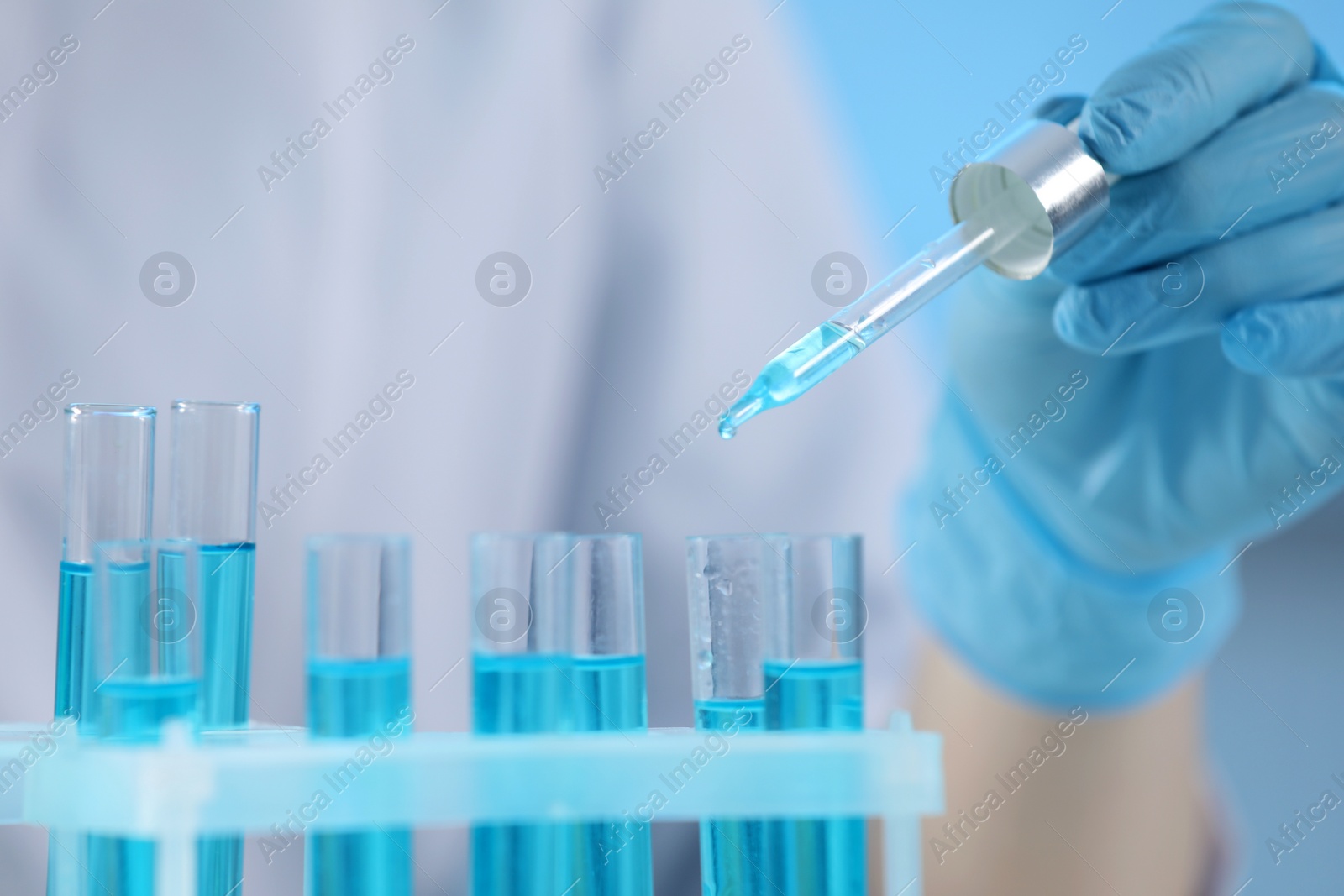 Photo of Scientist dripping liquid from pipette into test tube on blurred background, closeup